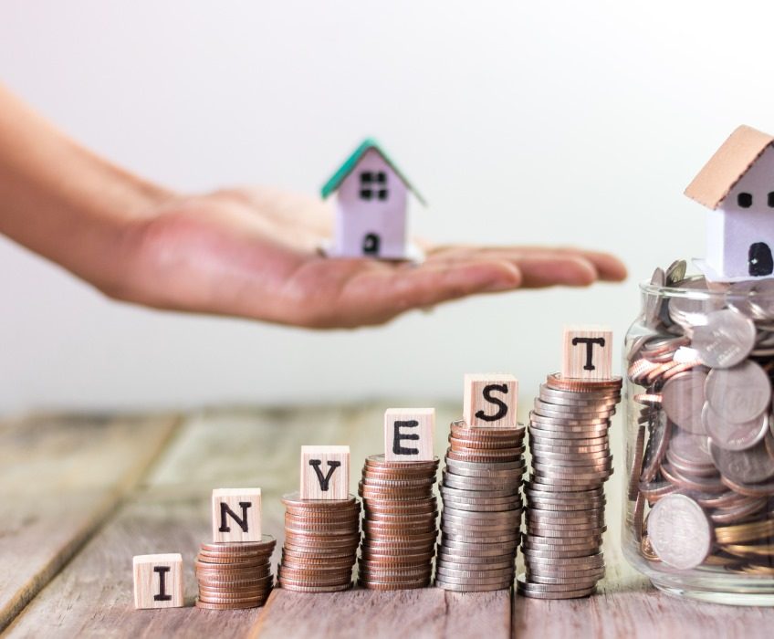 Stacked coins spelling “invest” with house models, representing property investment, wealth building, and financial planning with Innovest advisers in New Zealand.